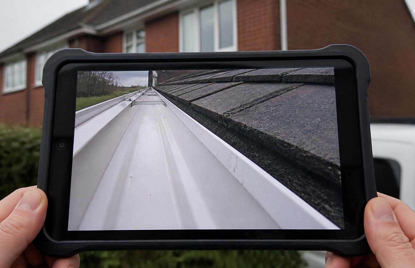 Tablet screen showing wireless pole camera footage of a cleared gutter run on a Warwickshire home