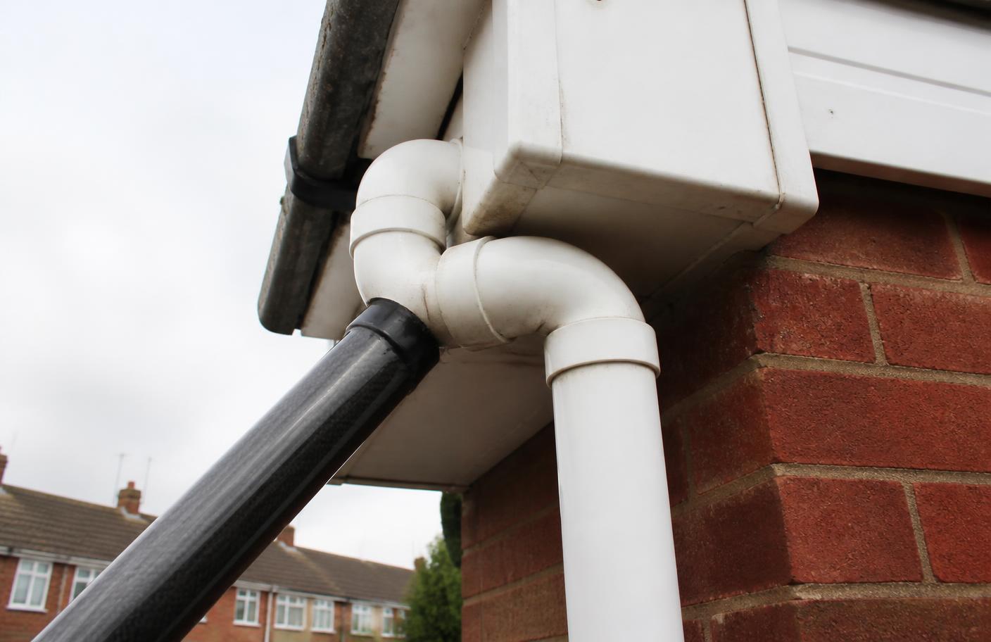 Carbon fibre vacuum pole positioned at the swan neck bend of a uPVC downpipe on a red brick semi-detached house