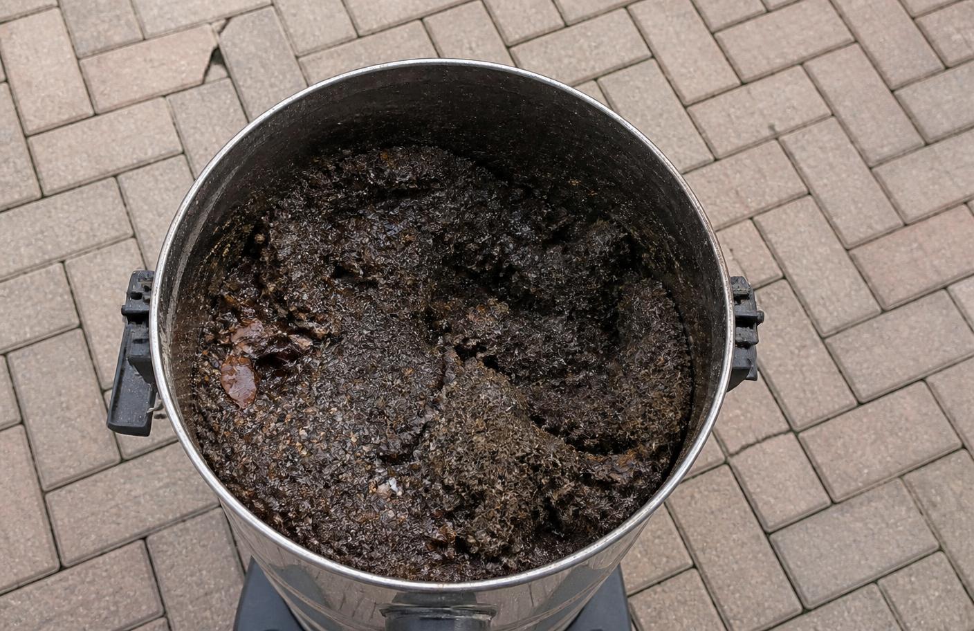 Open gutter vacuum collection drum showing wet silt, decomposed leaves and moss captured from a gutter clean